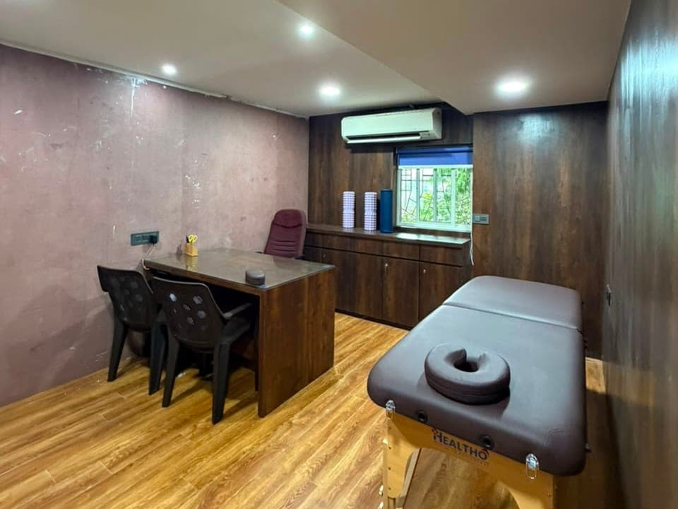 A consultation room set up with a desk, chairs and a treatment plinth